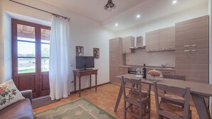 A modern kitchen with wooden cabinets, a dining table with chairs, a TV on a wooden stand, and a view through a glass door. - FARMHOUSE QUERCETO - APARTMENT OLIVE TREE (Gubbio)