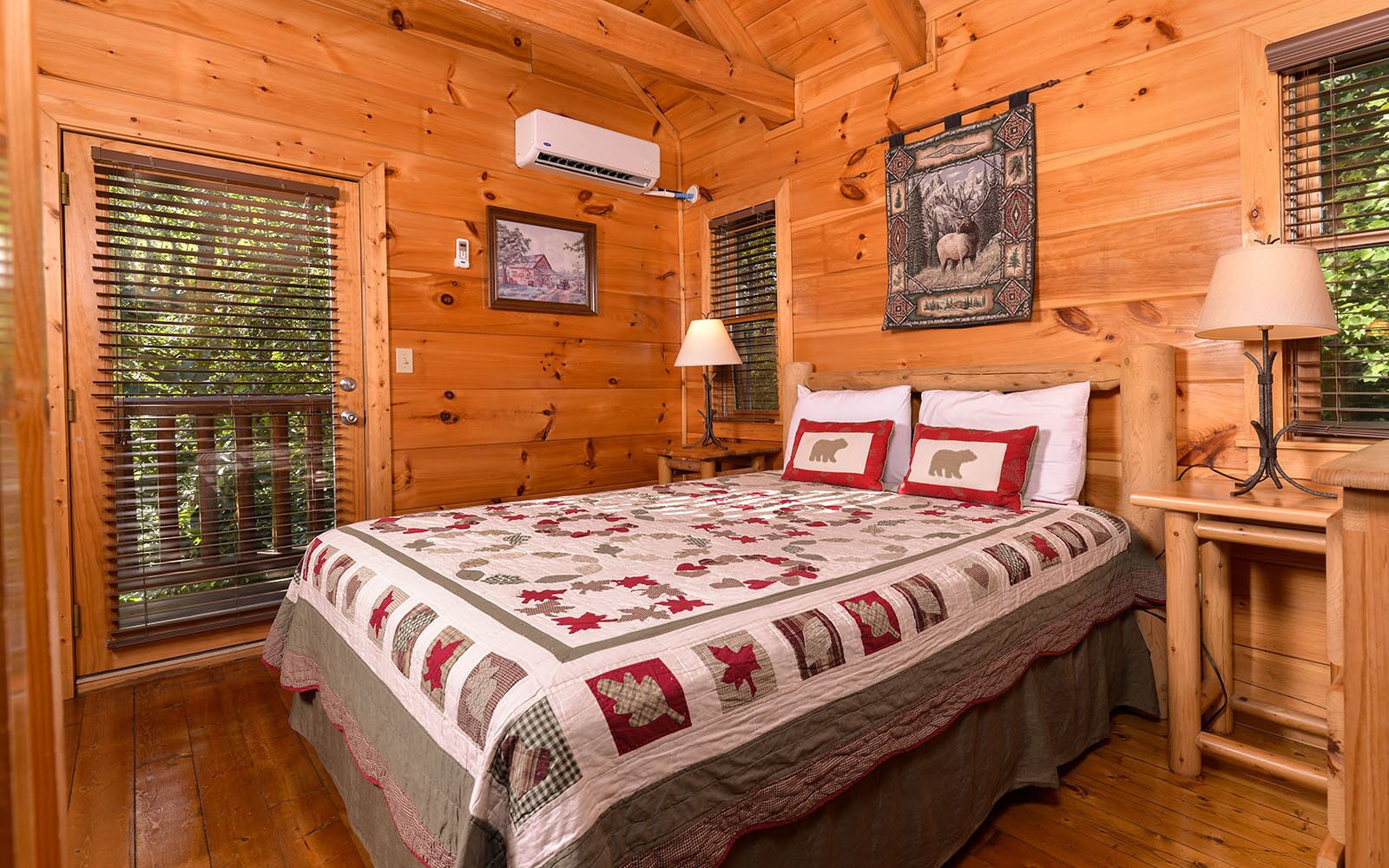 A cozy wooden cabin bedroom with a bed, a nightstand, a lamp, and a window with blinds.