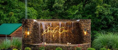 Un mur de pierre avec une cascade, et les mots « Smoky Cove » illuminés au centre.