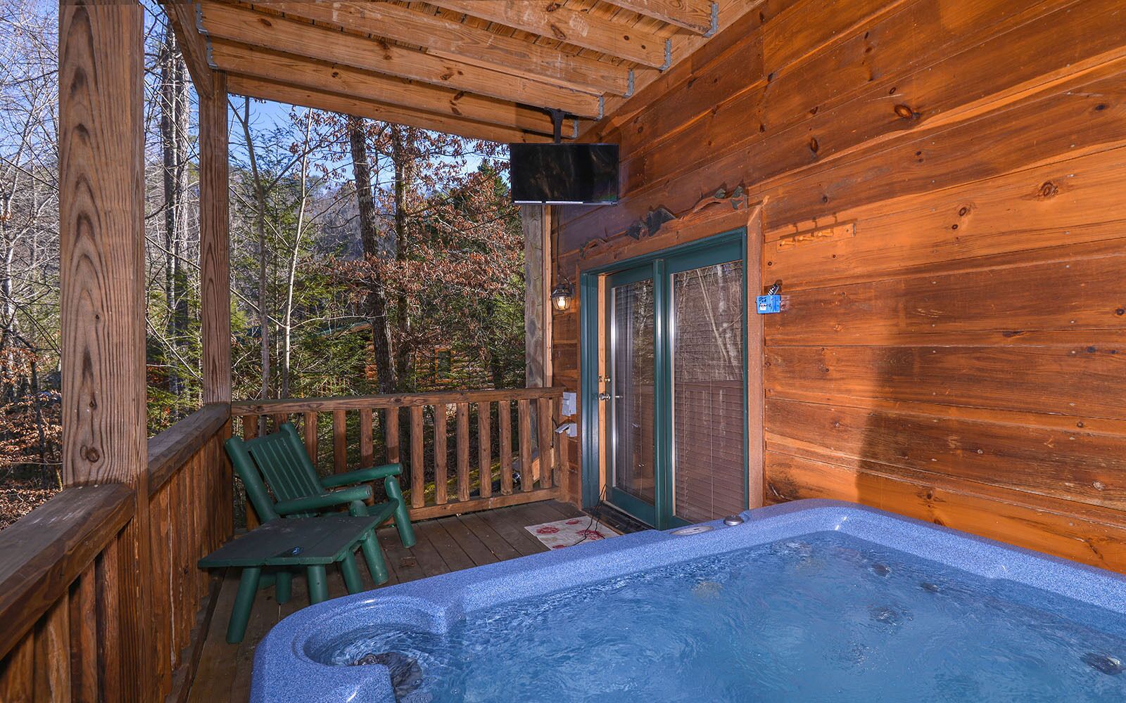 A wooden cabin with a hot tub, a door with a glass panel, and a chair outside.