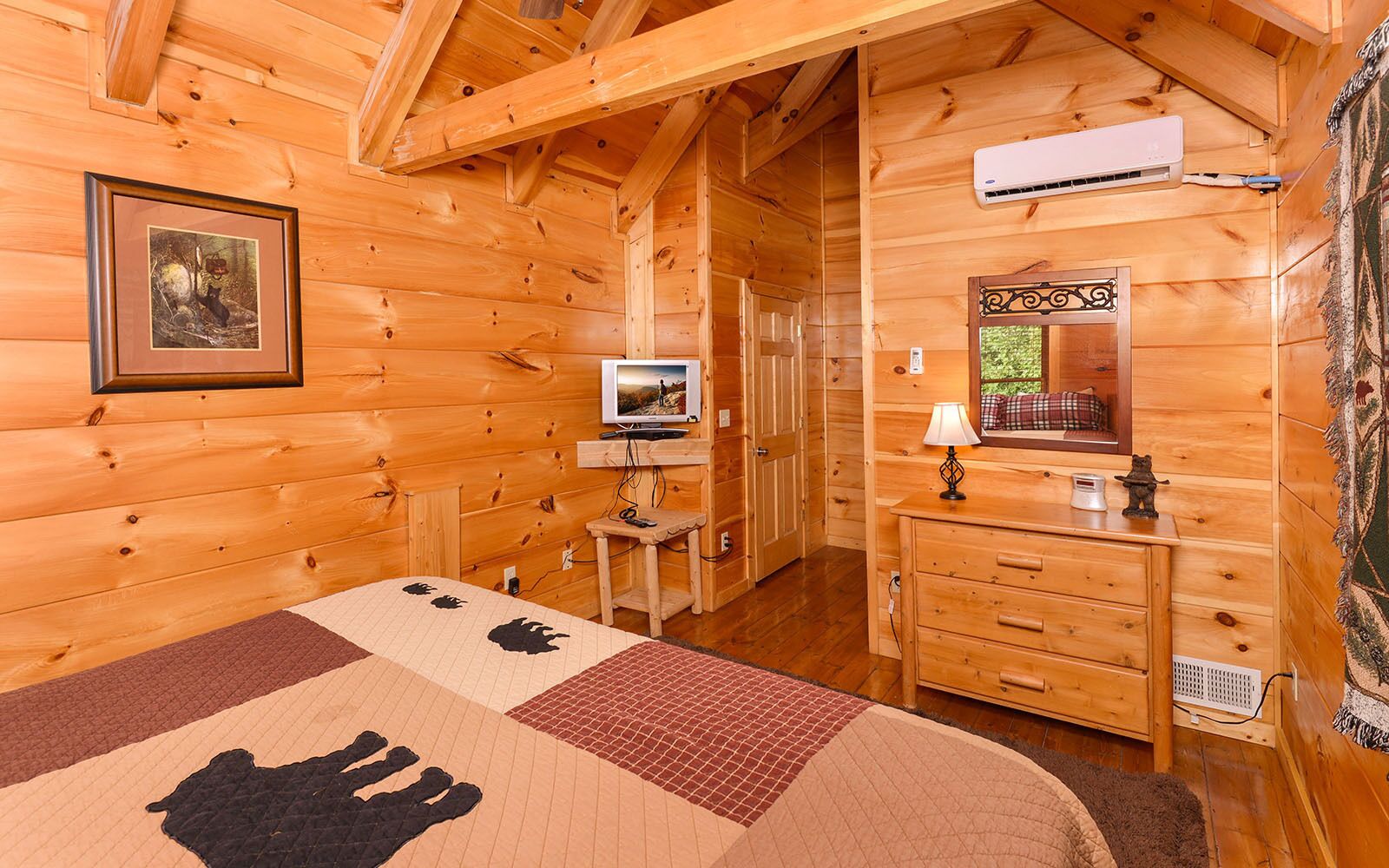 A cozy log cabin room with a bed, dresser, television, and a framed picture on the wall.
