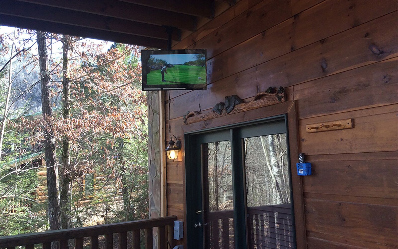 A wooden cabin with a TV mounted on the wall, a door with a nameplate, and a porch with a railing.