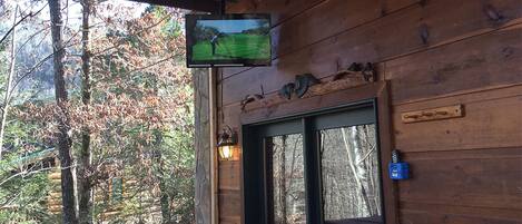 A wooden cabin with a TV mounted on the wall, a door with a nameplate, and a porch with a railing.
