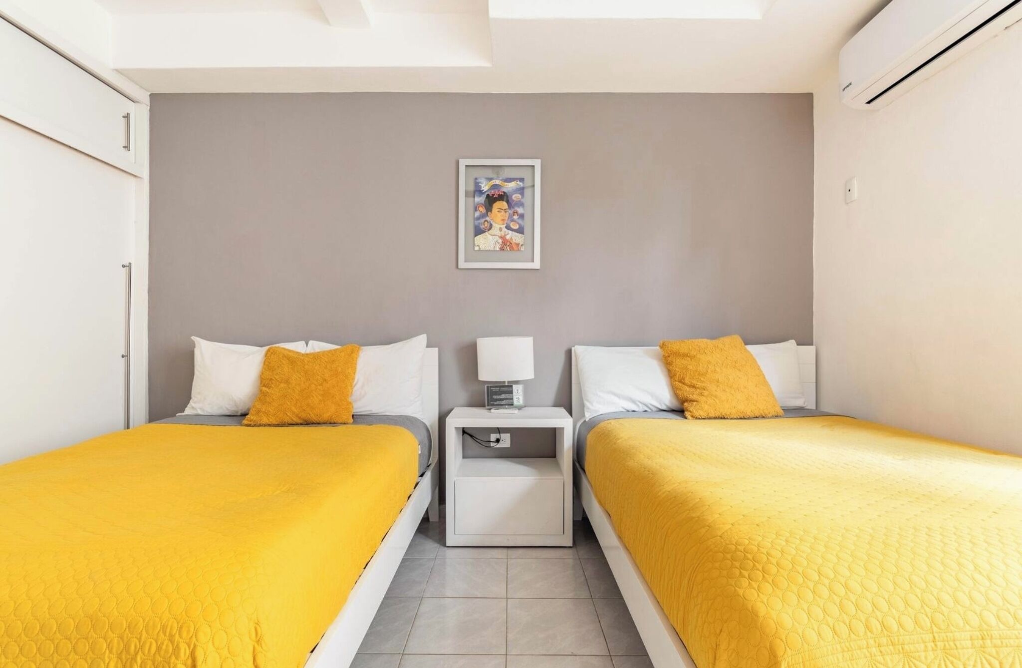 A hotel room with two beds, a nightstand, a bedside table, and a framed picture on the wall.