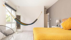 Ein Schlafzimmer mit einer Hängematte, einem Bett mit gelber Decke, einem Stuhl und einem Nachttisch mit Lampe.