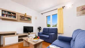 A modern living room with a sofa, a TV, a bookshelf, and a dining table with a fruit bowl.