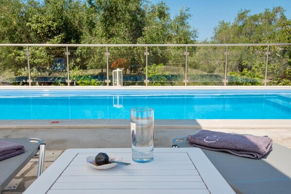 A poolside area with a glass of water, a bowl of food, and towels on lounge chairs.