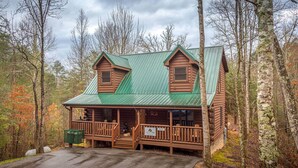 Eine Blockhütte mit einem grünen Metalldach, einer Veranda mit Holzgeländern und einem Schild, das einen Campingplatz kennzeichnet.