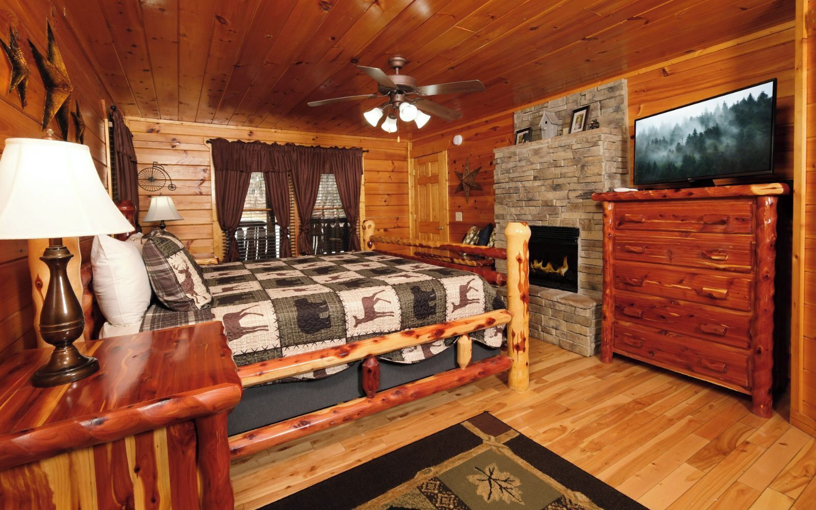 A cozy log cabin room with a bed, wooden dresser, fireplace, and a television.