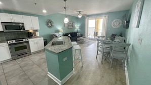 A modern kitchen with a central island, a dining area with a table and chairs, and a living room with a sofa.