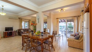 A spacious living area with a dining table, chairs, a sofa, and a TV. - Villa Jan Lui - Four Bedroom Villa, Sleeps 8 (Argaka)