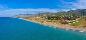 Vista aérea de una zona costera con playa, casas y colinas al fondo.
