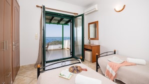 A bedroom with two beds, a wooden wardrobe, a bathroom with a mirror, and a balcony with a view.