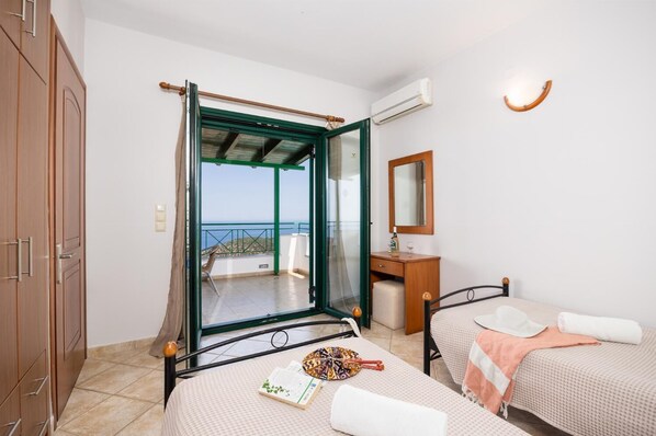 A bedroom with two beds, a wooden wardrobe, a bathroom with a mirror, and a balcony with a view.