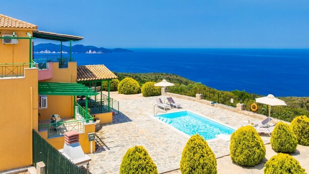 A pool area with a view of the sea, a staircase, and a building with a green roof.