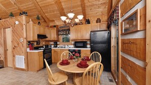 Cocina de cabaña de madera con una mesa de comedor para cuatro, un refrigerador negro y armarios de madera.