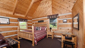Una habitación tipo cabaña de madera con una cama de madera, un escritorio, una silla y una ventana con vistas al exterior.