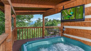 Una terraza de madera con un jacuzzi, un televisor montado en la pared y vistas al exterior.