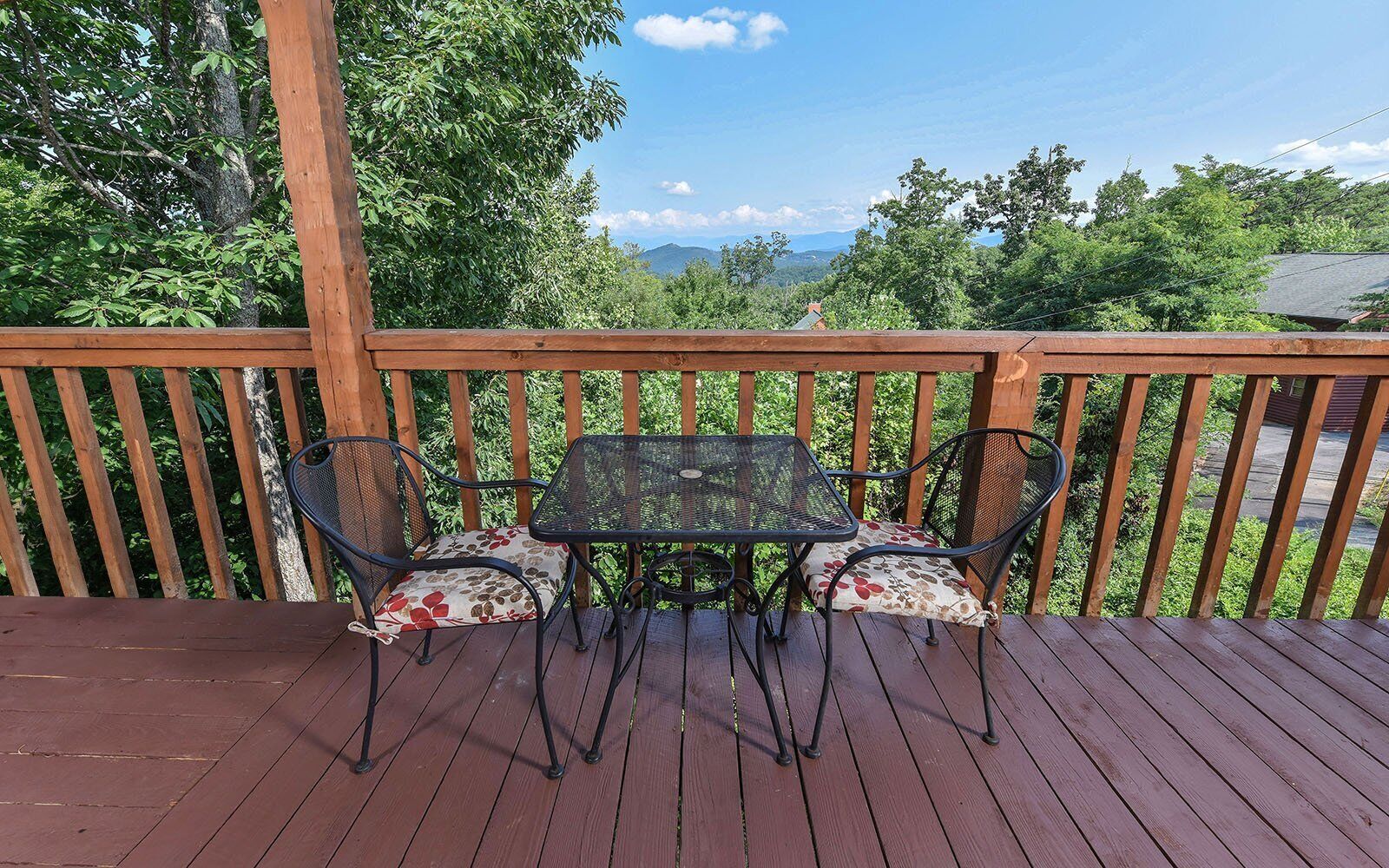 Eine Holzterrasse mit Tisch und Stühlen, die einen schönen Ausblick auf eine Landschaft mit Bäumen und Bergen bietet.