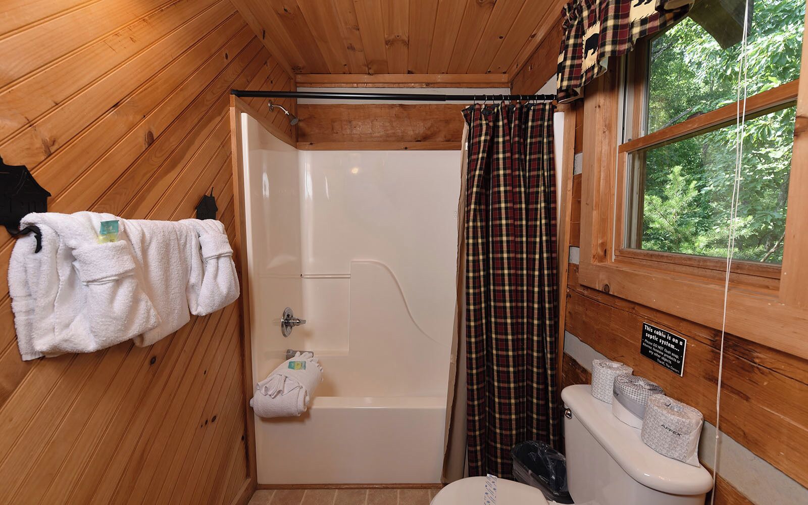 A cabin bathroom with a shower, toilet, and a window with a view of trees.