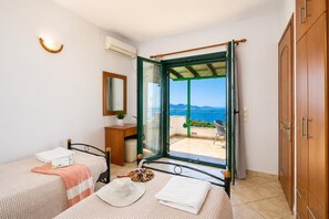 Een slaapkamer met twee bedden, een spiegel, een nachtkastje, een kledingkast en een balkon met uitzicht op zee.