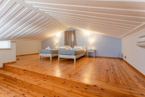 Une chambre avec deux lits, un plancher en bois, un plafond en pente et une fenêtre.