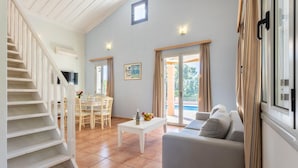 Un vaste espace de vie comprenant un escalier, une table à manger pour quatre personnes, un canapé et une vue sur une piscine, visible à travers des portes vitrées.