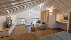 A spacious loft with a high ceiling, a staircase, a sofa, a coffee table, and a TV.