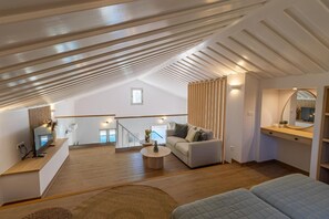 Ein geräumiger Loft mit hohen Decken, einer Treppe, einem Sofa, einem Couchtisch und einem Fernseher.