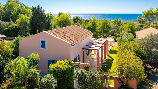 A two-story house with a tiled roof, surrounded by lush greenery and a clear view of the sea.