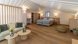 A spacious loft bedroom with a high ceiling, a large bed, a sofa, a round coffee table, and a wardrobe.