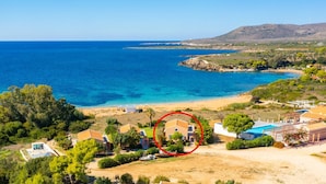 En fastighet vid kusten med ett stort hus omgivet av grönska, en strand och utsikt över havet.