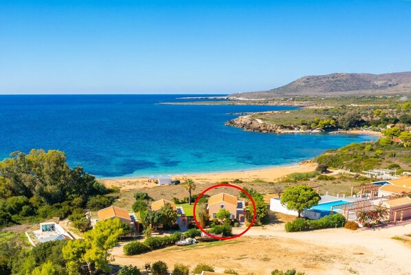 Una propiedad costera con una casa grande rodeada de vegetación, una playa y vistas al mar.