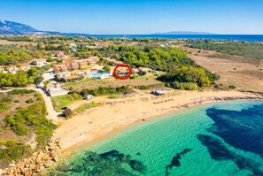 Vista aérea de uma área costeira com praia, águas azuis cristalinas e um complexo residencial com vários edifícios e piscina.