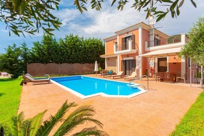 A two-story house with a swimming pool, outdoor furniture, and a fenced garden.