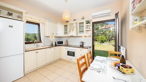 Une cuisine moderne avec des meubles blancs, une table à manger dressée pour deux personnes et une vue sur un jardin, visible à travers la porte vitrée.