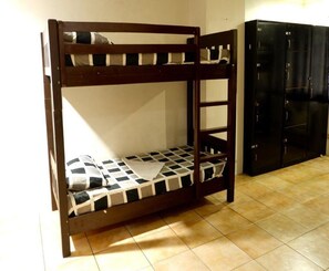Un lit superposé avec un matelas à carreaux, une armoire noire et un sol carrelé.