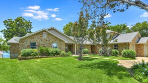 A two-story stone house with a well-maintained lawn and a small tree in the front yard.