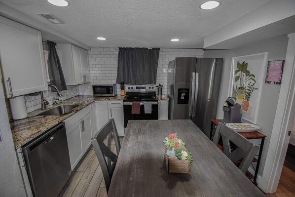 A modern kitchen with white cabinets, stainless steel appliances, and a wooden dining table with a potted plant.