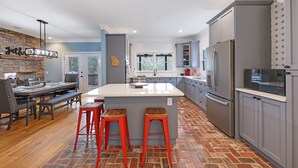 A modern kitchen with a large island, grey cabinets, and red bar stools. - 4.9-Star Rated, Stunning 3600 SF House on Golf Course (Waleska)