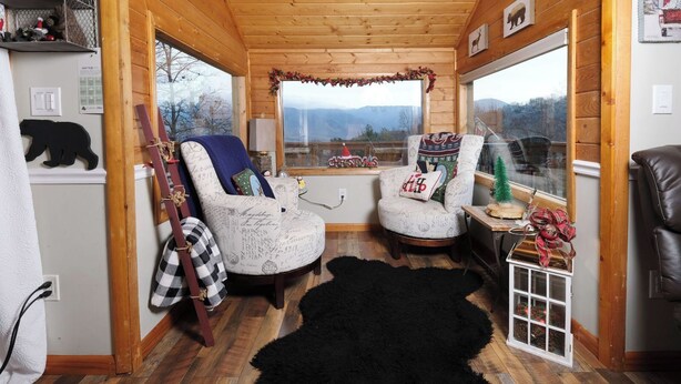 Interior acogedor de una cabaña con dos sillones tapizados, un felpudo negro y un árbol de Navidad.