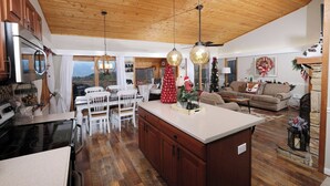 Una cocina amplia con armarios de madera, un comedor con sillas blancas, una isla central y una sala de estar acogedora con chimenea.