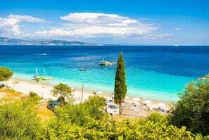 Ein Küstenstrand mit klarem türkisblauem Wasser, Booten und Strandsonnenschirmen.
