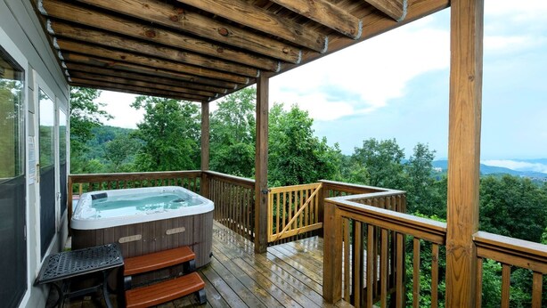 Een houten terras met een jacuzzi en een bank, met uitzicht op een bebost gebied.