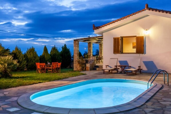 Una piscina con terraza de piedra, mobiliario exterior y una pérgola.
