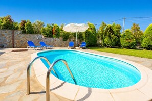 Une piscine bordée d’un muret en pierre, avec des chaises longues bleues et un parasol.