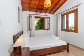 Un dormitorio con una cama de madera, una mesita de noche, una lámpara, una ventana con cortinas y vistas al exterior.