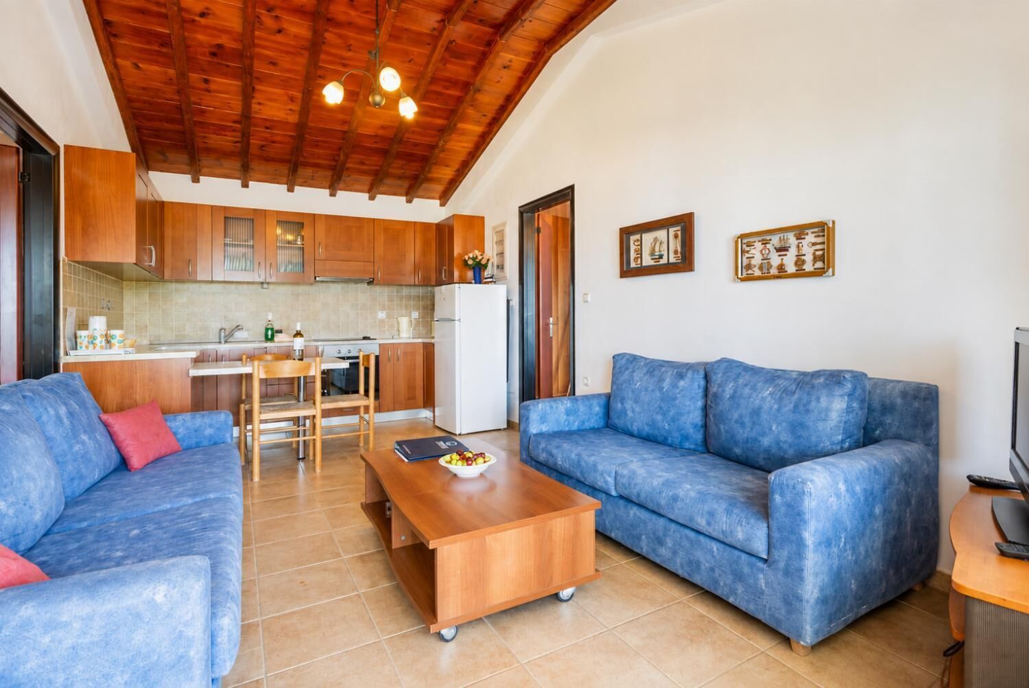 Ein Wohnzimmer mit einem blauen Sofa, einem Holztisch und einem Fernseher auf einem Holzschrank.