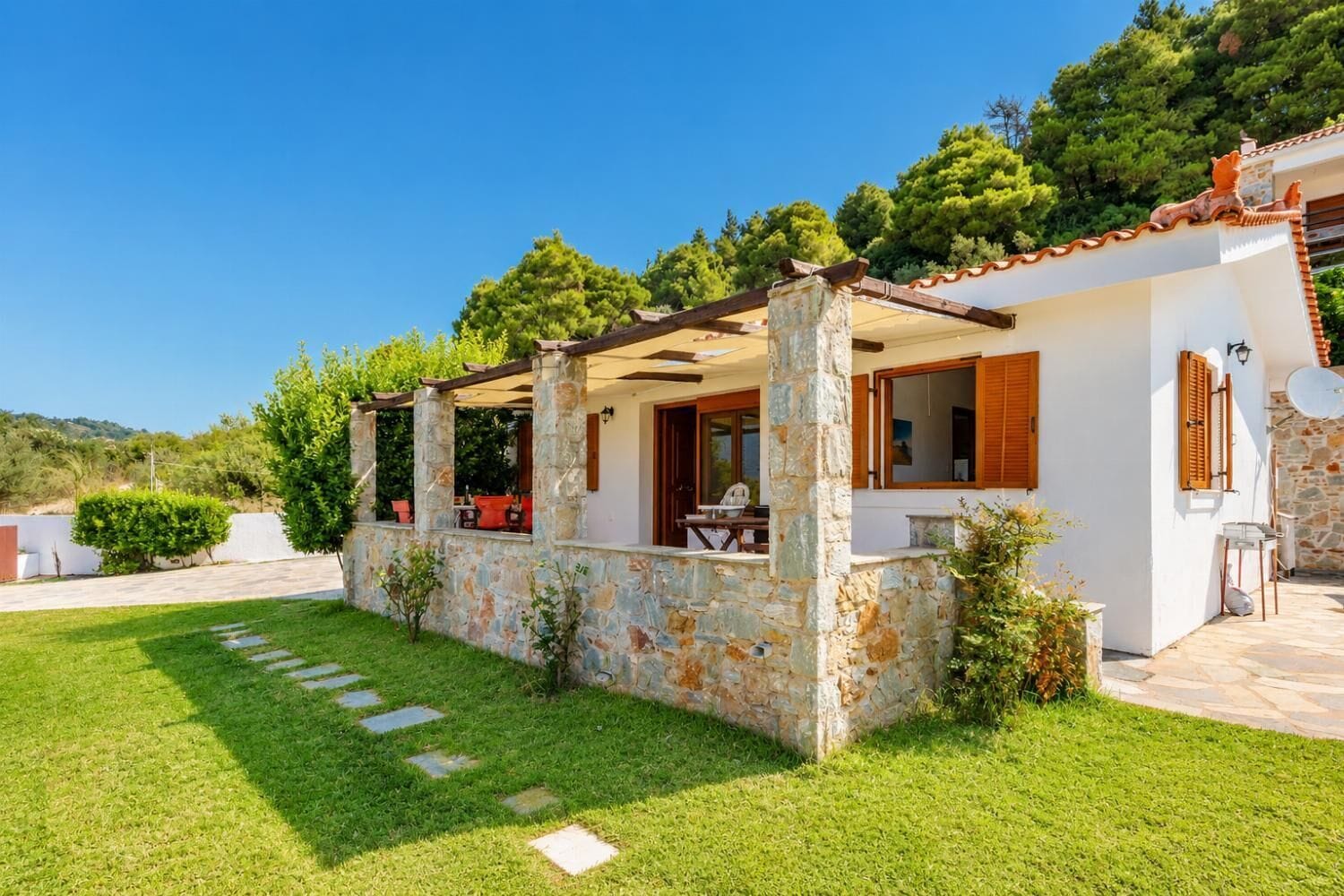 A house with a stone exterior, a covered patio, and a lawn.