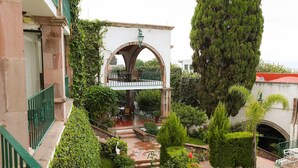 A courtyard with a central archway, a staircase, and a seating area with tables and chairs. - Posada la Ermita (San Miguel de Allende)